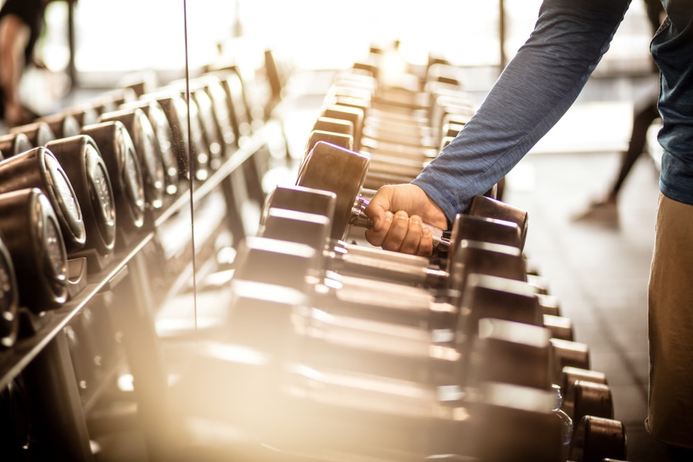 Man reaching for dumbbell in gym for strength training session.
