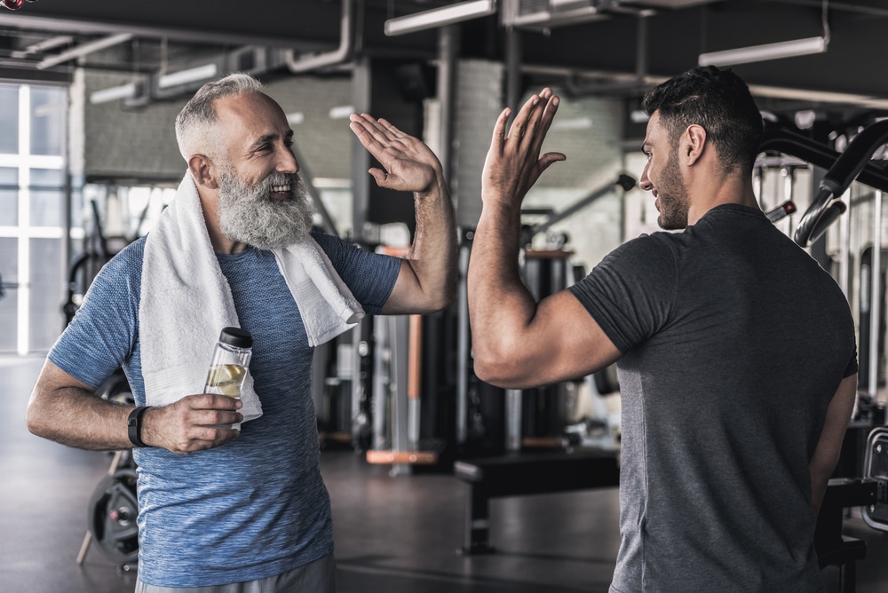 Senior man and personal trainer high-fiving at the gym
