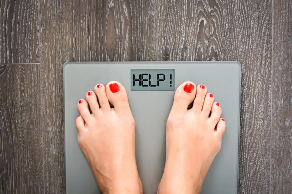 Feet standing on a scale displaying the word "HELP!"